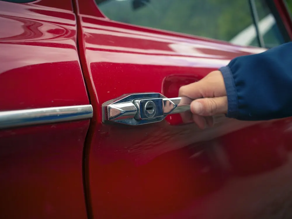 Main ouvrant la portière d'une voiture rouge